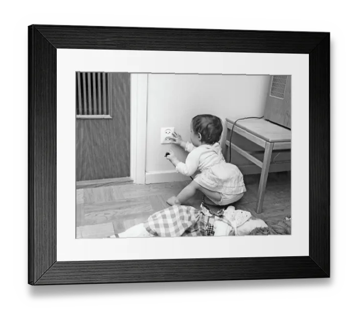Framed Print : Dangerous in the 1960s. A child is sitting on the floor and is curious about the electrical outlet in the wall. She holds a plug in one hand and fingers the outlet with the other Framed Print : Dangerous in the 1960s. A child is sitting on the floor and is curious about the electrical outlet in the wall. She holds a plug in one hand and fingers the outlet with the other
