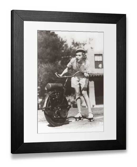 Framed Print : In the 1930s. A woman on roller skates holds on the handlebars of a one-wheel motorcycle that pulls her forward. She looks focused when the speed picks up