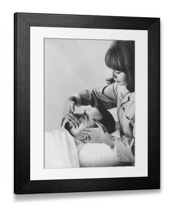 Framed Print : Beauty care 1967. A young woman is applying a cream or soap on a man's face