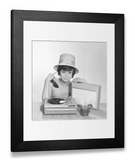 Framed Print : 1960s lifestyle. A young woman with a Philips radio and a gramophone as it could look in the summer. The summer hat, sun glasses and the cool drink glass is in the picture is added to get the right summer feeling in the studio