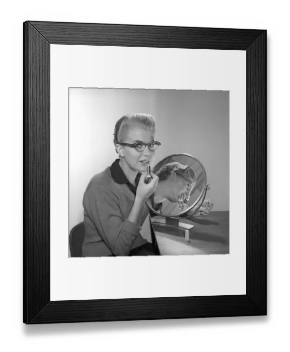 Framed Print : In the 1950s. A young woman with a mirror putting lipstick