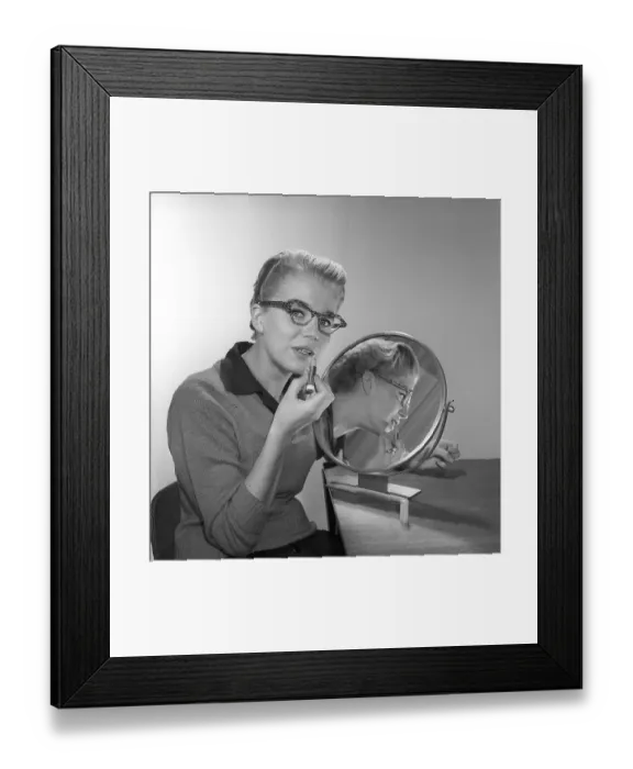 Framed Print : In the 1950s. A young woman with a mirror putting lipstick on. She has the glasses and bows typical of the 1950s. 1958. Kristoffersson ref CB99-12
