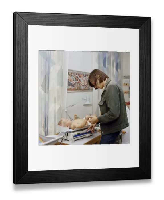 Framed Print : 1960s parents. A father at the childcare center is checking the weight of his son who is lying on the scales. 1969