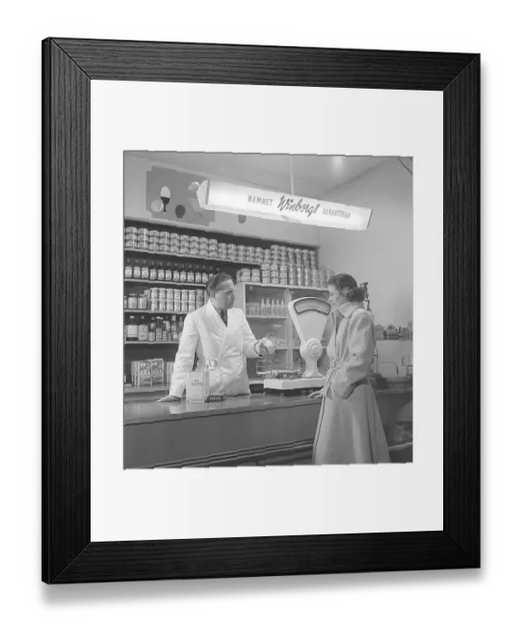 Framed Print : Woman in a grocery store in the 1940s A young woman stands at the counter where a merchant holds out a jar of rhubarb