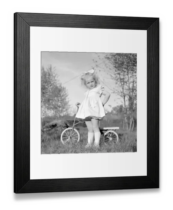 Framed Print : In the 1940s. A blonde little girl in a nice dress on her tricycle