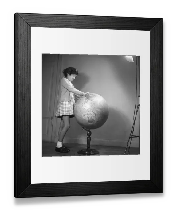 Framed Print : School in the 1940s. A girl in is very closely studying the details of a globe