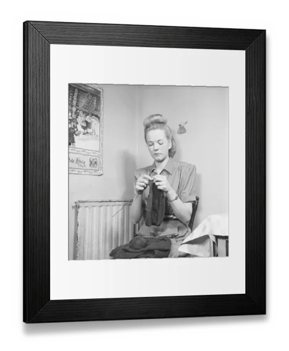 Framed Print : In the 1940s. A young woman sits in the kitchen on a chair and knits a sweater