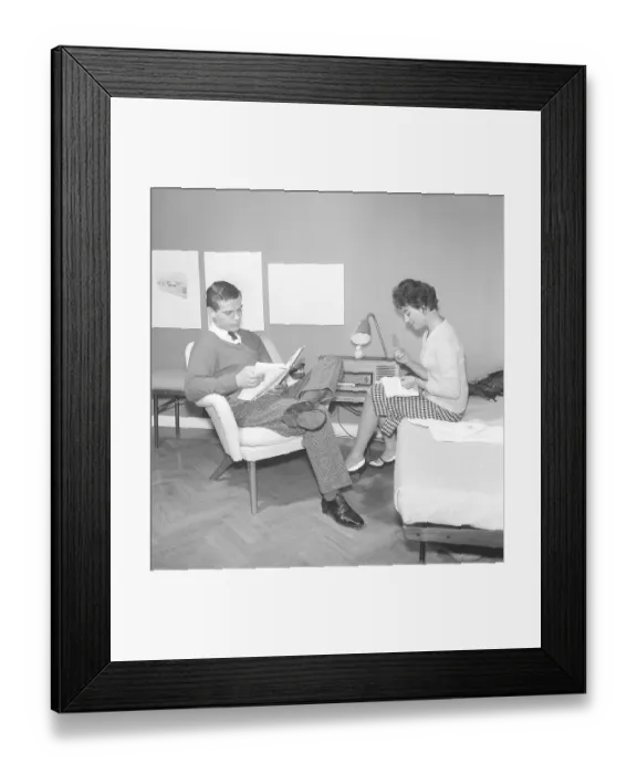Framed Print : A young couple sitting together at home in the 1950s. The man sits well dressed in shirt and tie reading while the young woman sits on the bed embroidering monograms on their bedclothes and pillowcases Framed Print : A young couple sitting together at home in the 1950s. The man sits well dressed in shirt and tie reading while the young woman sits on the bed embroidering monograms on their bedclothes and pillowcases