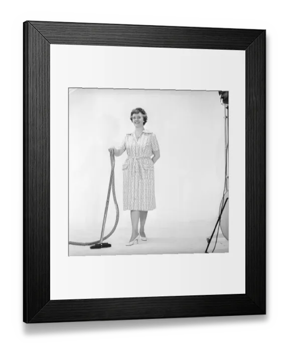Framed Print : Cleaning day in the 1960s. A woman is standing holding a vacuum cleaner Framed Print : Cleaning day in the 1960s. A woman is standing holding a vacuum cleaner