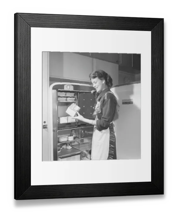 Framed Print : In the kitchen 1950s. Interior of a kitchen and a young woman standing at the Leonard refrigirator with it's door open, showing the cans and bottes of different food standing on the shelfes Framed Print : In the kitchen 1950s. Interior of a kitchen and a young woman standing at the Leonard refrigirator with it's door open, showing the cans and bottes of different food standing on the shelfes