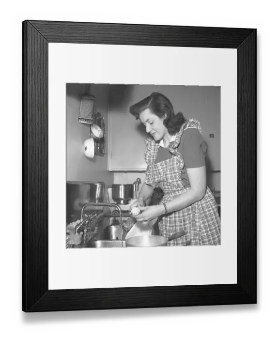 Framed Print : In the 1940s. A woman in a typical 1940s kitchen with the details of the interior and the objects being very representative of the decade