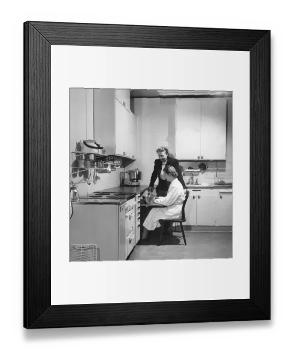 Framed Print : In the 1950s. Two women are seen in a typical 1950s kitchen with the details of the interior Framed Print : In the 1950s. Two women are seen in a typical 1950s kitchen with the details of the interior