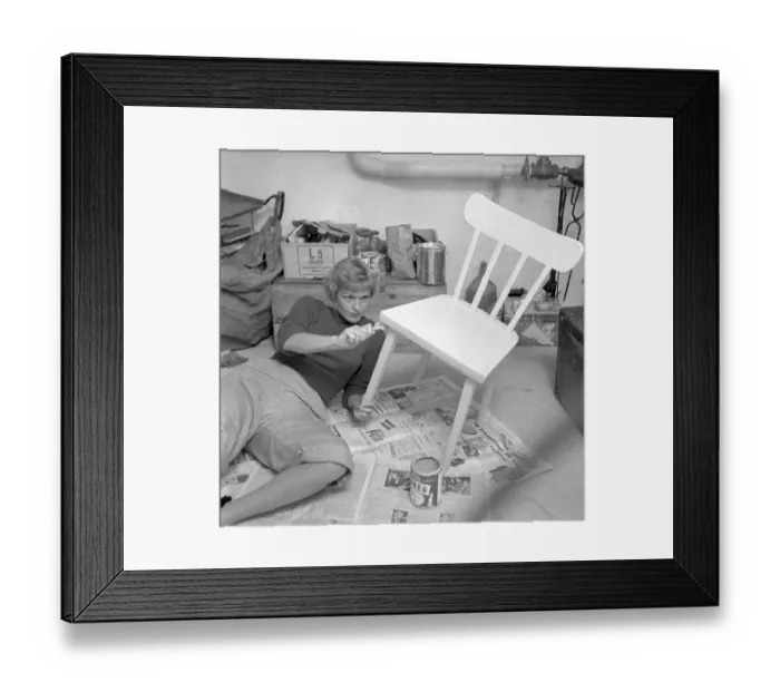 Framed Print : In the 1950s. A woman is seen painting a wooden chair in a bright color