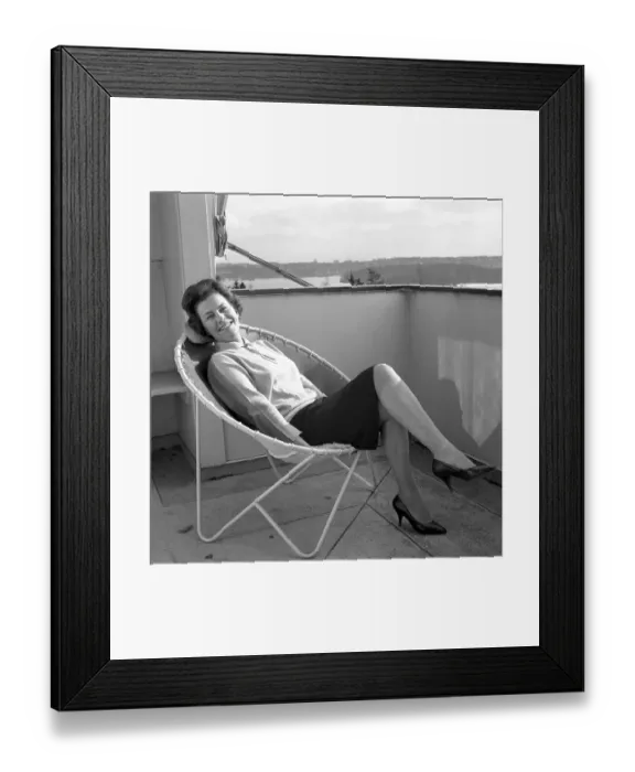 Framed Print : Home decor of the 1960s. A woman is sitting comfortably in the 1950s 1960s deck chair designed with steel pipes with a round center and four legs. The seat is made of leather Framed Print : Home decor of the 1960s. A woman is sitting comfortably in the 1950s 1960s deck chair designed with steel pipes with a round center and four legs. The seat is made of leather