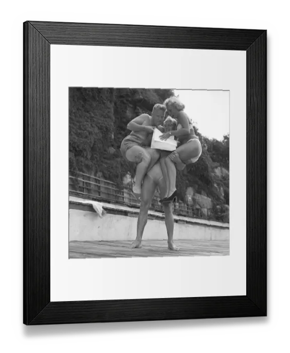 Framed Print : In the 1950s. The strong man have a woman and a man on each arm while reading a paper Framed Print : In the 1950s. The strong man have a woman and a man on each arm while reading a paper