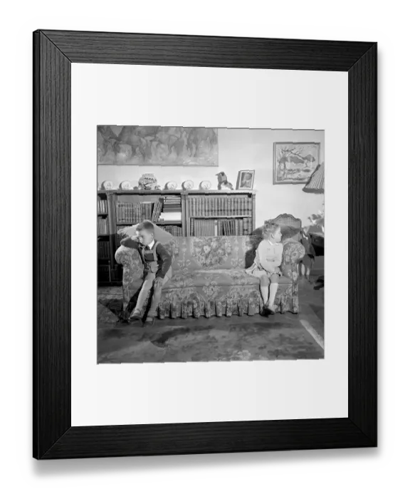 Framed Print : In the 1950s. Two children are sitting at the far ends of the sofa