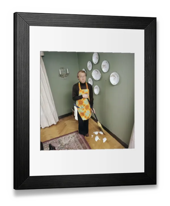 Framed Print : Cleaning day in the 1970s. An interior of a man cleaning the floor. Bits of a plate that used to hang on the wall is seen on the floor, he must have torn it down with the handle