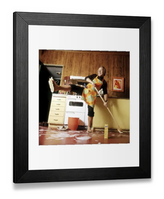 Framed Print : Cleaning day in the 1970s. An interior of a kitchen where a man is seen cleaning the floor
