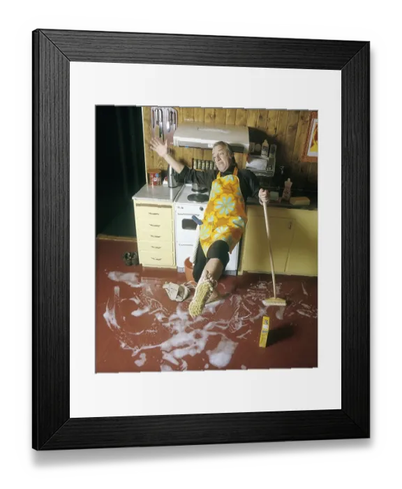 Framed Print : Cleaning day in the 1970s. An interior of a kitchen where a man is seen cleaning the floor