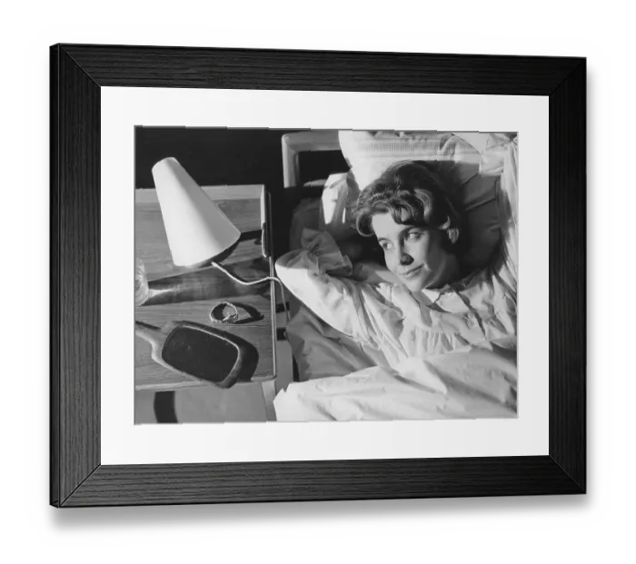 Framed Print : Sleep in the 1960s. A young woman lies comfortably ensconced in a bed