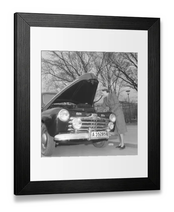 Framed Print : In the 1940s. A nicely dressed woman in a matching jacket and skirt has opened the hood of her Ford car