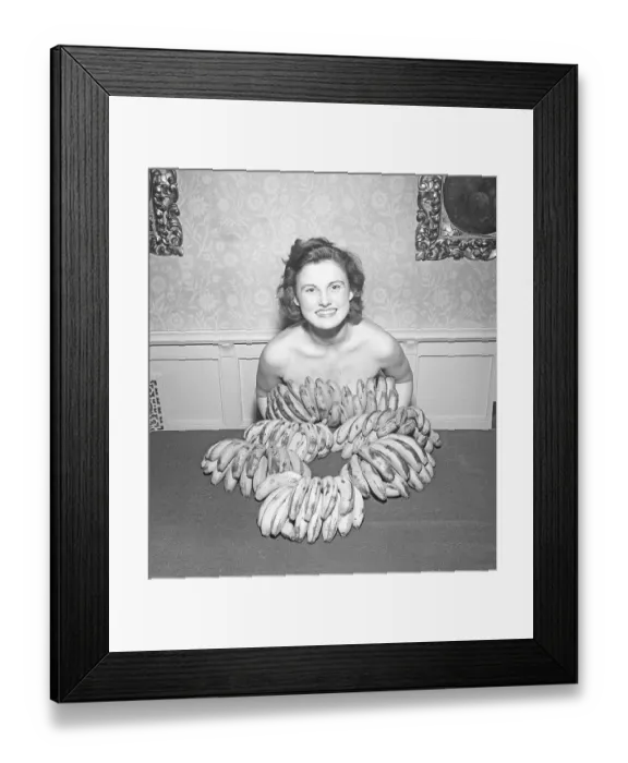 Framed Print : Going bananas in the 1950s. A young woman covers herself with bananas