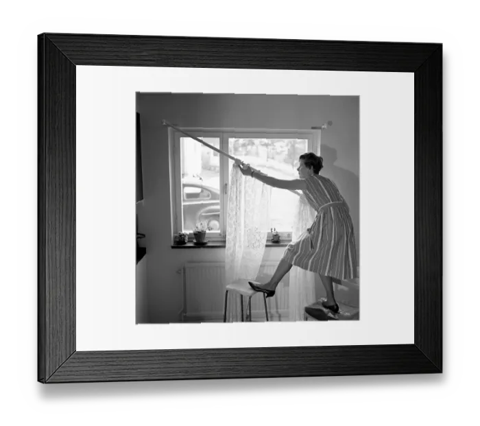 Framed Print : 1960s home decorating. A woman at home putting up the curtains in the room window. All by herself she balances on a chair and a stool to manage it. Sweden 1966 Framed Print : 1960s home decorating. A woman at home putting up the curtains in the room window. All by herself she balances on a chair and a stool to manage it. Sweden 1966