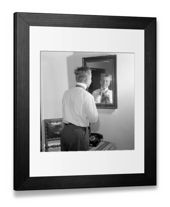 Framed Print : Getting dressed in the 1950s. A young man in front of the mirror knots his necktie