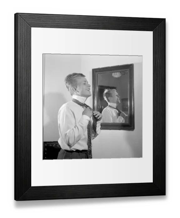 Framed Print : Getting dressed in the 1950s. A young man in front of the mirror knots his necktie Framed Print : Getting dressed in the 1950s. A young man in front of the mirror knots his necktie