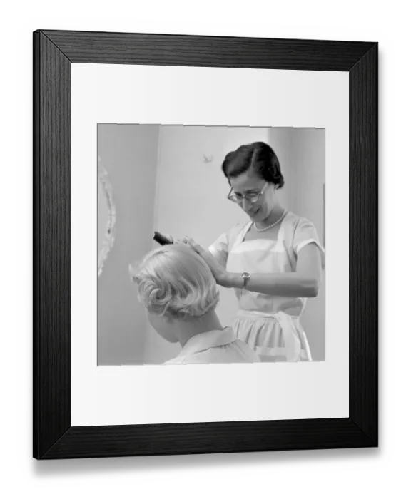 Framed Print : Getting a 1950s hairdo. A hairdresser is seen combing a blond woman's hair