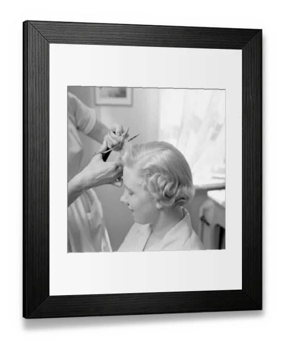 Framed Print : Getting a 1950s hairdo. A hairdresser is seen cutting the blond woman's hair shorter with a pair of scissors