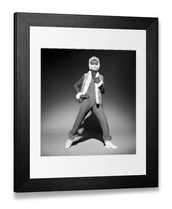 Framed Print : In the 1960s. A fashion model, in typical 1960s winter clothes in a studio. She has a thin overall on top over a knitted long sleeved sweater together with a vest, gloves and cap. Sweden 1966