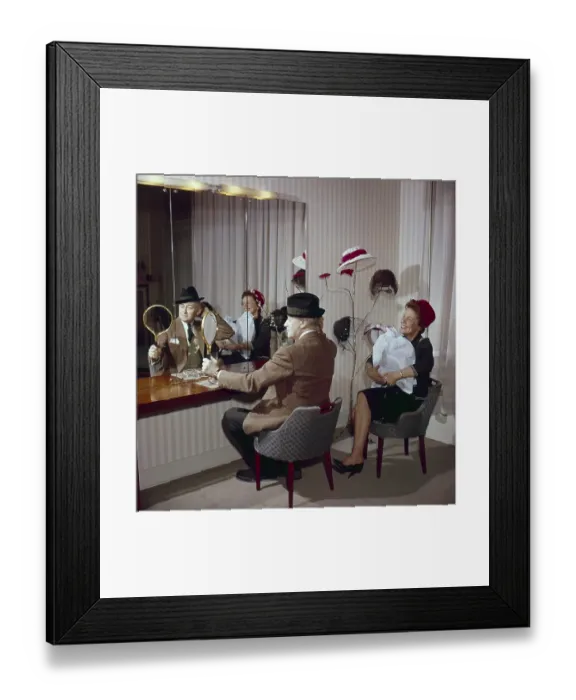 Framed Print : Trying out hats in the 1950s. A couple is sitting in front of a mirror trying hats