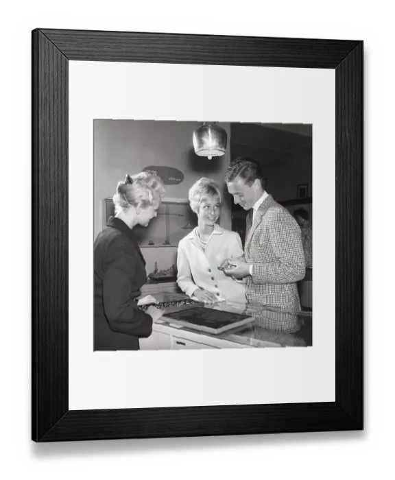 Framed Print : Love in the 1950s. A young couple at a jewelry shop is selecting wedding rings. A female sales clerk is standing at the counter with a case of many different models of rings. Kristoffersson ref CG35 Framed Print : Love in the 1950s. A young couple at a jewelry shop is selecting wedding rings. A female sales clerk is standing at the counter with a case of many different models of rings. Kristoffersson ref CG35