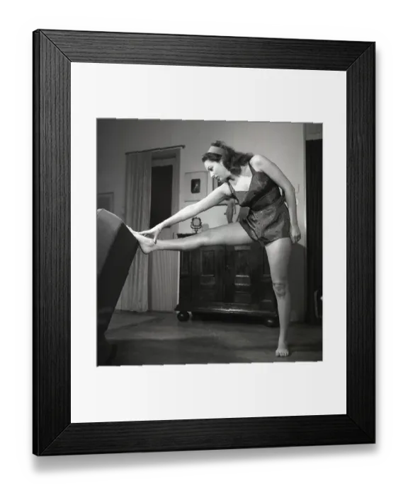 Framed Print : In the 1940s. A young woman in her livingroom while exercising Framed Print : In the 1940s. A young woman in her livingroom while exercising