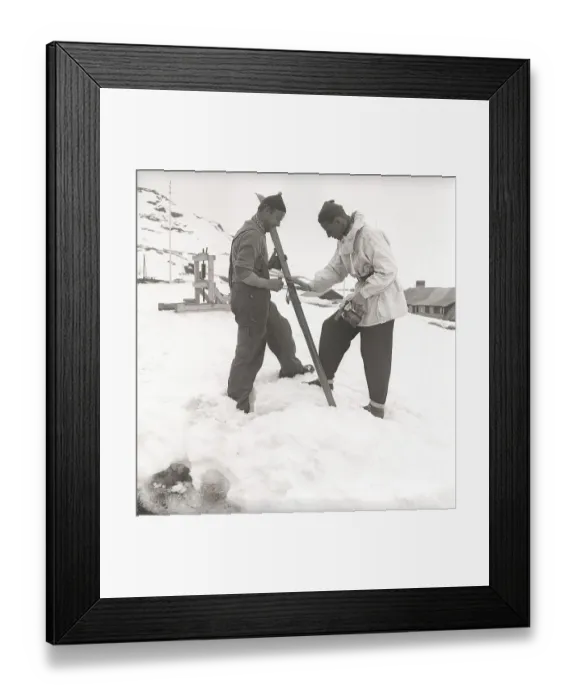 Framed Print : Winter in the 1940s. Two men are going skiing and prepares the skis with ski wax to get better traction on the snow