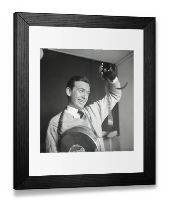 Framed Print : Film interest in the 1950s. A man holding a roll of film is looking at the frames to see what's on it Framed Print : Film interest in the 1950s. A man holding a roll of film is looking at the frames to see what's on it