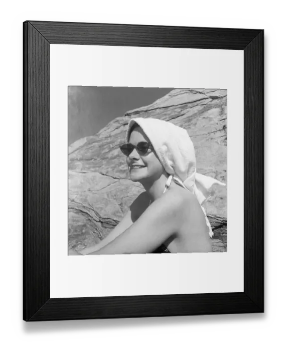 Framed Print : 1950s on the beach. A young woman on the beach takes extra care not to burn herself in the sun