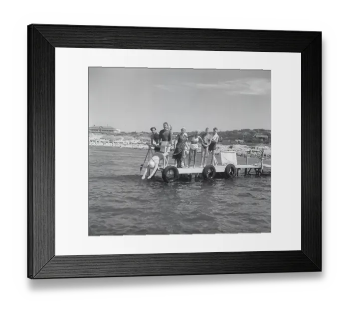 Framed Print : 1950s on the beach. Sunny day by the seaside and people standing looking when a woman dives into the water