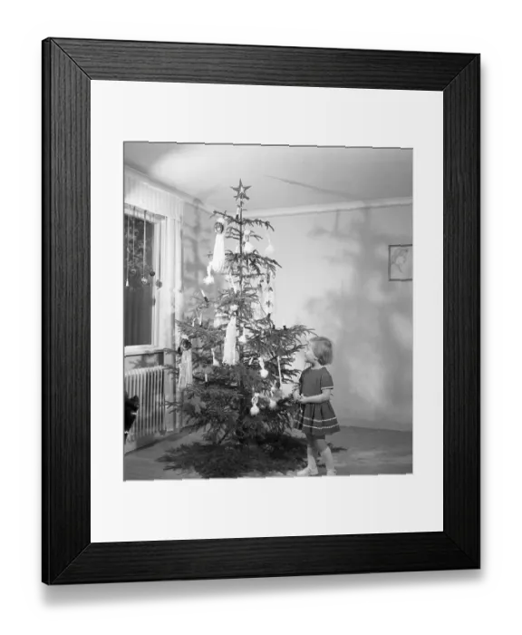 Framed Print : Christmas in the 1950s. A young girl is standing by the christmas tree