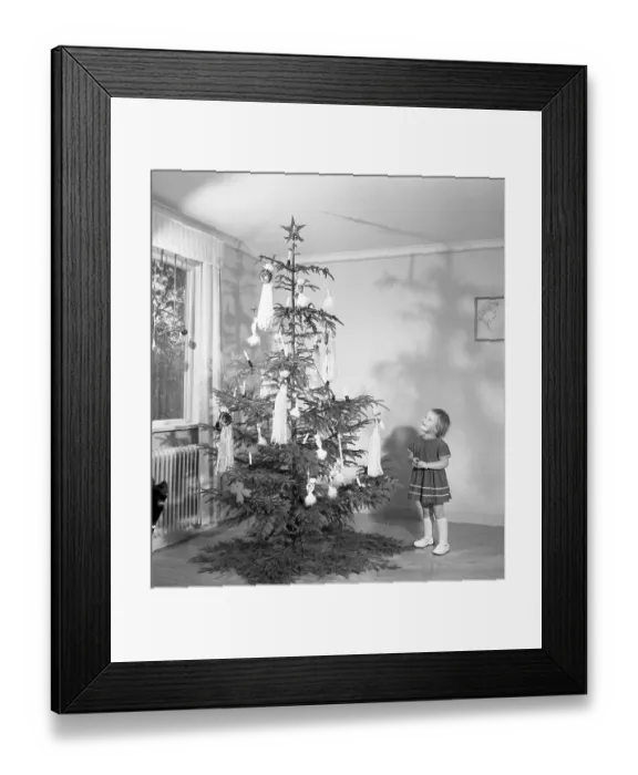 Framed Print : Christmas in the 1950s. A young girl is standing by the christmas tree