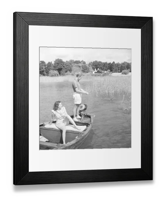 Framed Print : Fishing in the 1940s. A man is fishing from the boat and his girlfriend is enjoying the sun while waiting for him to catch a fish. The outboard motor is made by swedish manufacturer Penta Framed Print : Fishing in the 1940s. A man is fishing from the boat and his girlfriend is enjoying the sun while waiting for him to catch a fish. The outboard motor is made by swedish manufacturer Penta