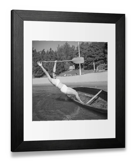 Framed Print : 1940s summer. A young woman has made attempt to stand up in a wonky canoe