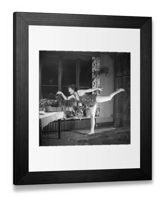 Framed Print : Woman of the 1940s. A woman is seen practising gymnastics while watering the plants in her apartment