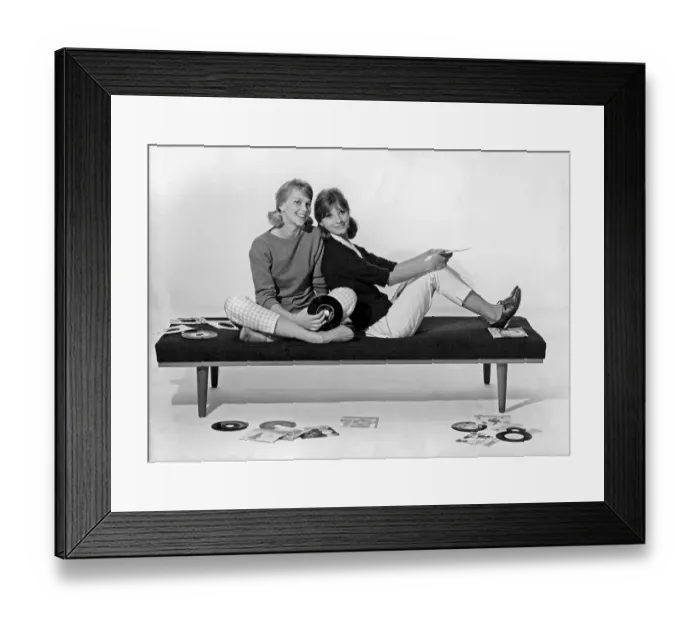 Framed Print : 1960s lifestyle. Two girls in typical 1960s clothes are sitting together holding music records