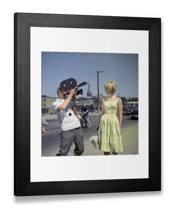 Framed Print : A young blonde woman is being filmed by a man with a film camera Framed Print : A young blonde woman is being filmed by a man with a film camera
