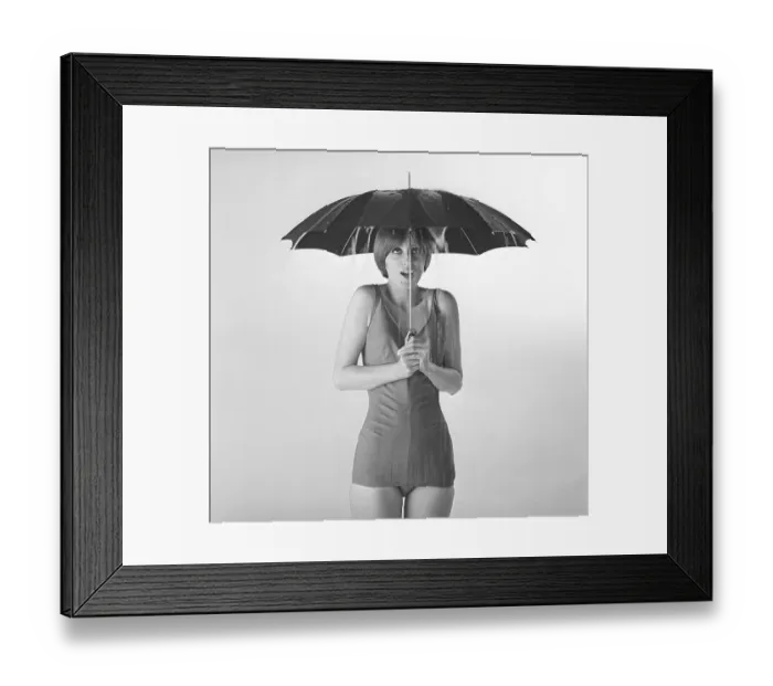 Framed Print : 1960s woman. A young woman in a bathing suit is standing under an umbrella