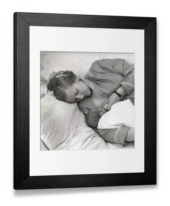 Framed Print : 1950s mother nursing her baby. A young woman breastfeeding her baby while lying in bed at home