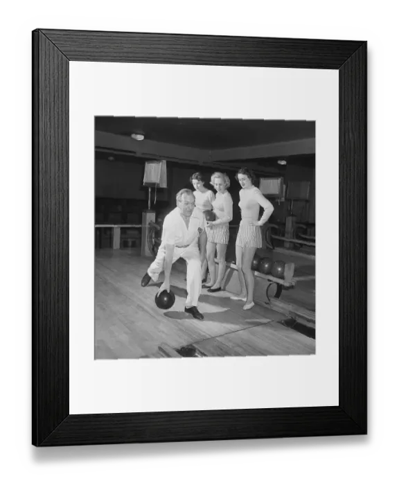Framed Print : Bowling in the 1950s. A man is throwing the bowling ball and three young women are standing beside and looking. they are dressed in short striped skirts and jumpers