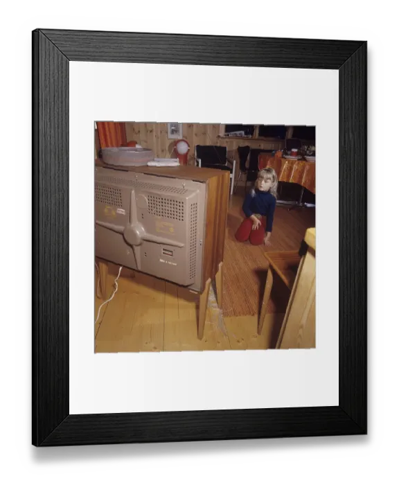 Framed Print : Television in the 1960s. A girl is sitting in front of a television set with her eyes on the screen and the program